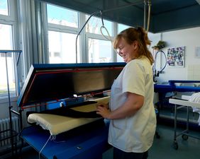 Wäscherei-Mitarbeiterin Katrin R. an einem XXL-Dampfbügeleisen, mit dem Kittel und andere Wäschestücke geglättet werden.